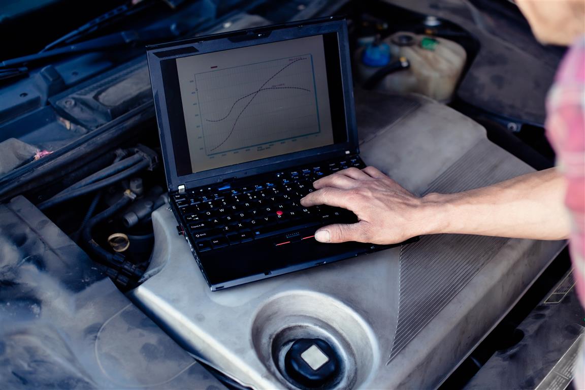 Car mechanic with laptop checking enine